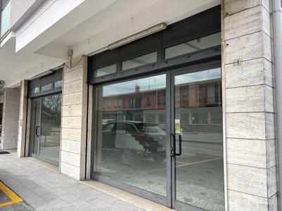Unità commerciale ad uso negozio su due livelli, piano terra e rialzato, facente parte di un fabbricato condominiale di n. 3 piani complessivi fuori terra; presenta ampie vetrine sui lati est e nord, con due porte di accesso, sgombra di arredi. Internamente è composta: negozio, retro-negozio (accessibile da piccola scala interna), spogliatoio, antibagno, WC, magazzino. Non risulta occupato.