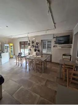 Piena proprietà di porzione di edificio (con contestuale vendita di residua parte a Lotto 2) costituita da unità immobiliare ad uso commerciale (osteria/bar) di 120 mq. Accesso da scala esterna o rampa per disabili sul fronte; unità composta da: vano principale bar; cucina con uscita secondaria sul retro; sala da pranzo; disimpegno, ripostiglio; doppi servizi igienici.Impianto di riscaldamento centralizzato non funzionante (il bar è munito di stufa a pellet); resede esterno (comune) per parcheggio; pozzo. 